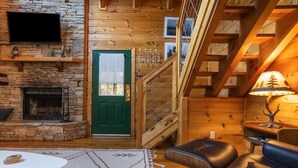 Ein gemütliches Blockhaus-Interieur mit Kamin aus Stein, einer grünen Tür, einer Treppe und einem Ledersofa.