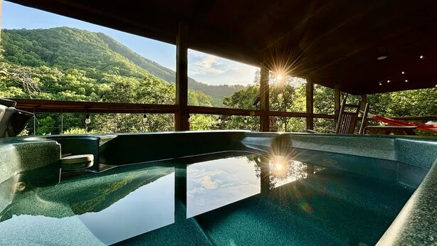 Ein Wellnessbereich mit Pool, Holzterrasse und Blick auf eine gebirgige Landschaft.