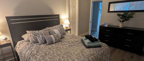 A bedroom with a bed, a ceiling fan, a nightstand, a dresser, and a wall-mounted TV.