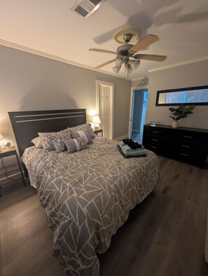 Ein Schlafzimmer mit Bett, Deckenventilator, Nachttisch, Kommode und Wandfernseher.