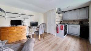 A compact living space with a kitchenette, a dining area with a table and chairs, a television, and a sofa. - Studio Retreat Sleeps 1 - WiFi & Parking (Cambridge)