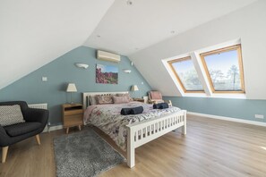 A bedroom with a sloped ceiling, a bed with floral bedding, a nightstand, a chair, and a window with a view of trees. - 2-Bed Cottage Devon/Cornwall border - Dog-friendly (Newbridge, Gunnislake)