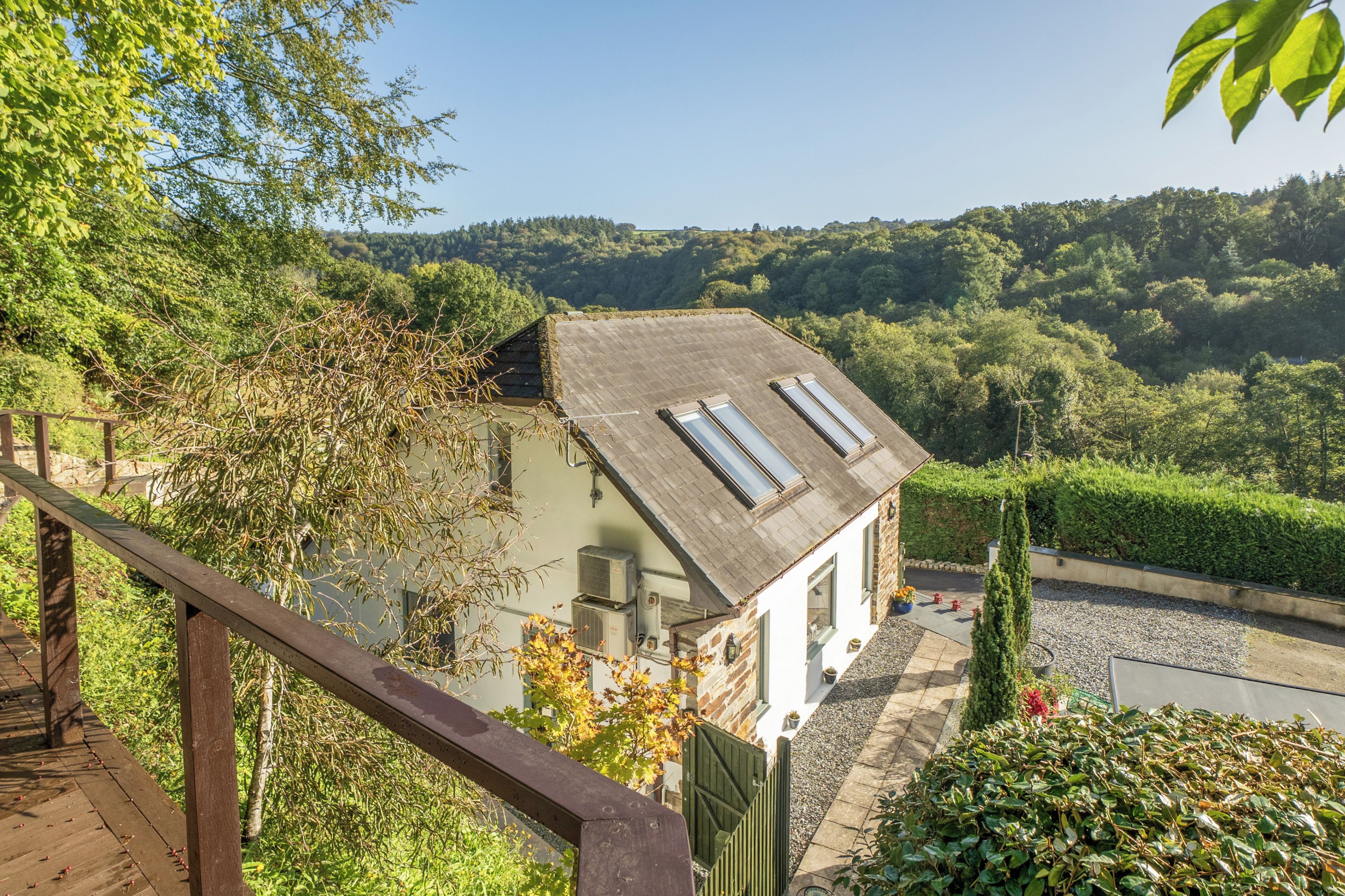 A house with a sloped roof, a wooden deck, and a view of a forested valley.