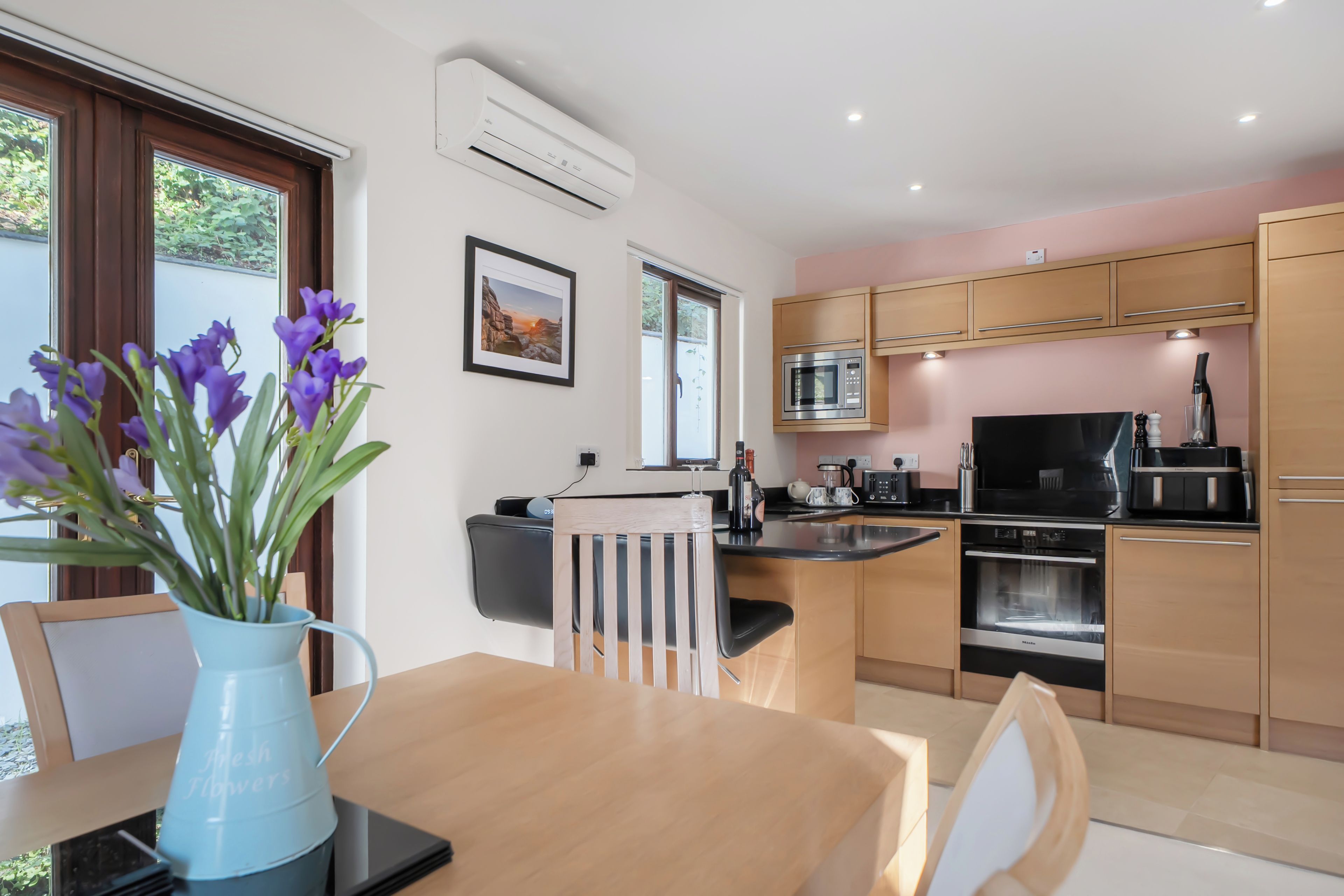 A modern kitchen with a dining area, featuring a built-in microwave, oven, and a coffee machine.