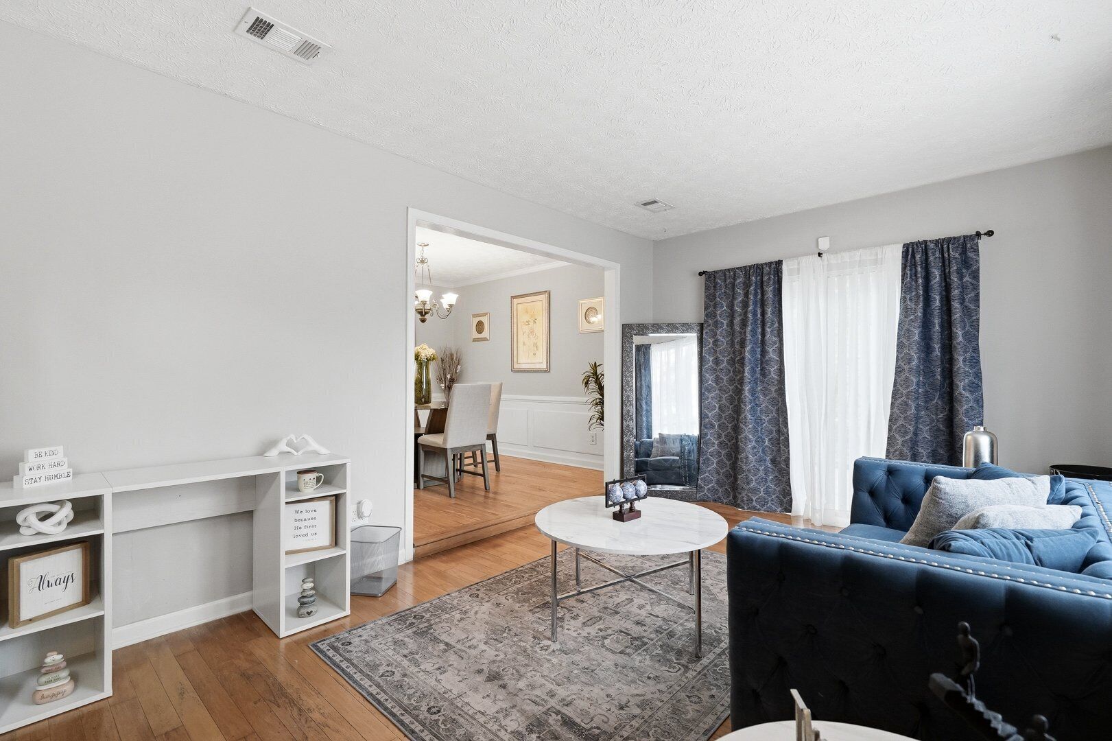 A modern living room with a blue sofa, a white coffee table, and a dining area with a chandelier.