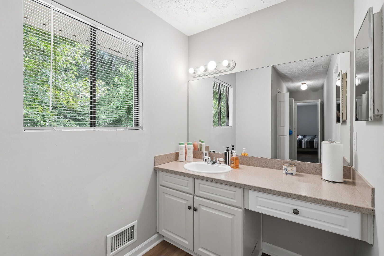 Une salle de bain équipée d’un lavabo, d’un meuble-vasque, d’un miroir et d’une fenêtre avec des stores.