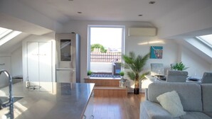 Eine moderne Küche mit einer großen Kochinsel, einem Essbereich mit einer Couch und Blick durch ein großes Fenster.