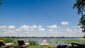 Blick auf einen See mit einer Holzsteg, Liegestühlen und einer Bank.