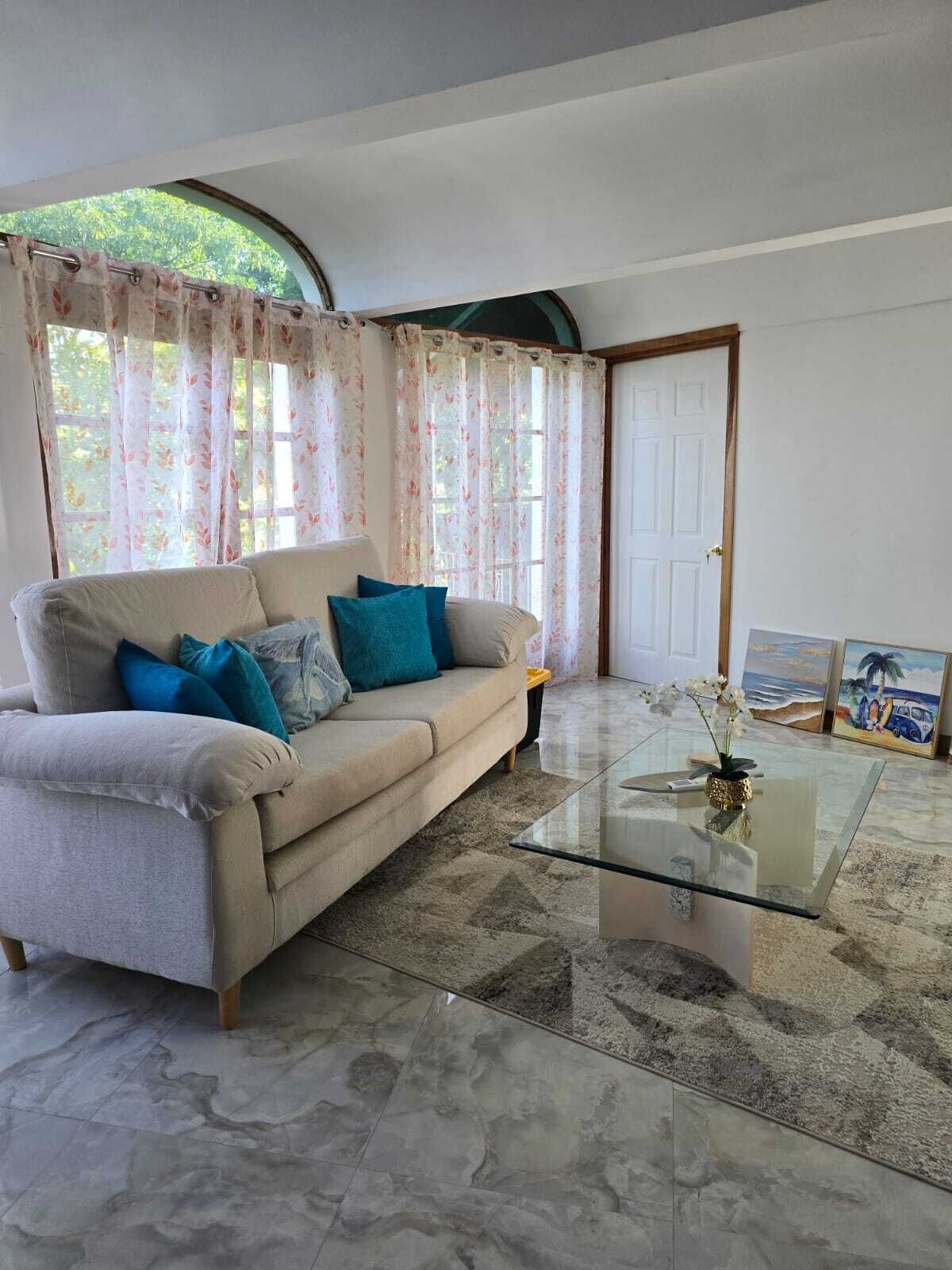 A living room with a sofa, a glass coffee table, and a door.