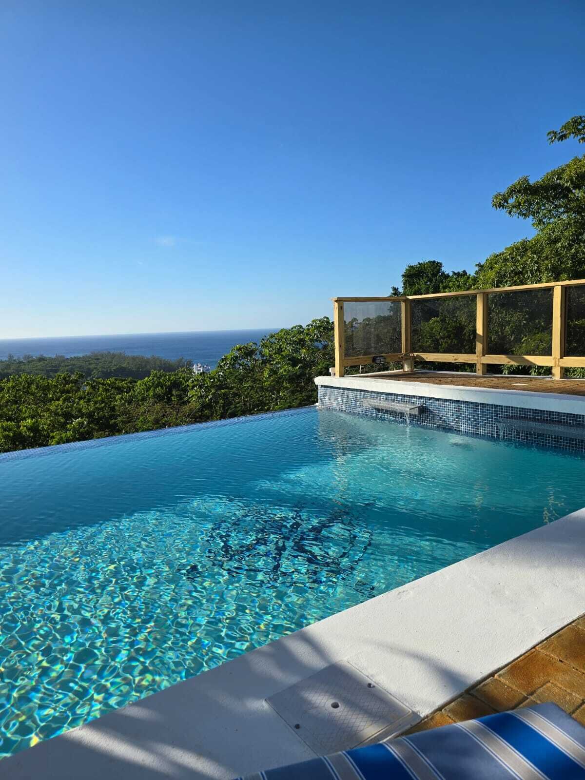 A clear blue pool with a view of the ocean and a wooden deck.