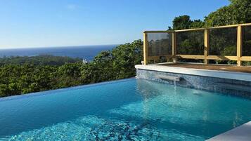 A clear blue pool with a view of the ocean and a wooden deck.