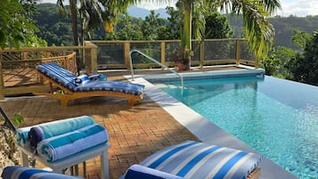 A poolside area with lounge chairs and a view of palm trees and hills.