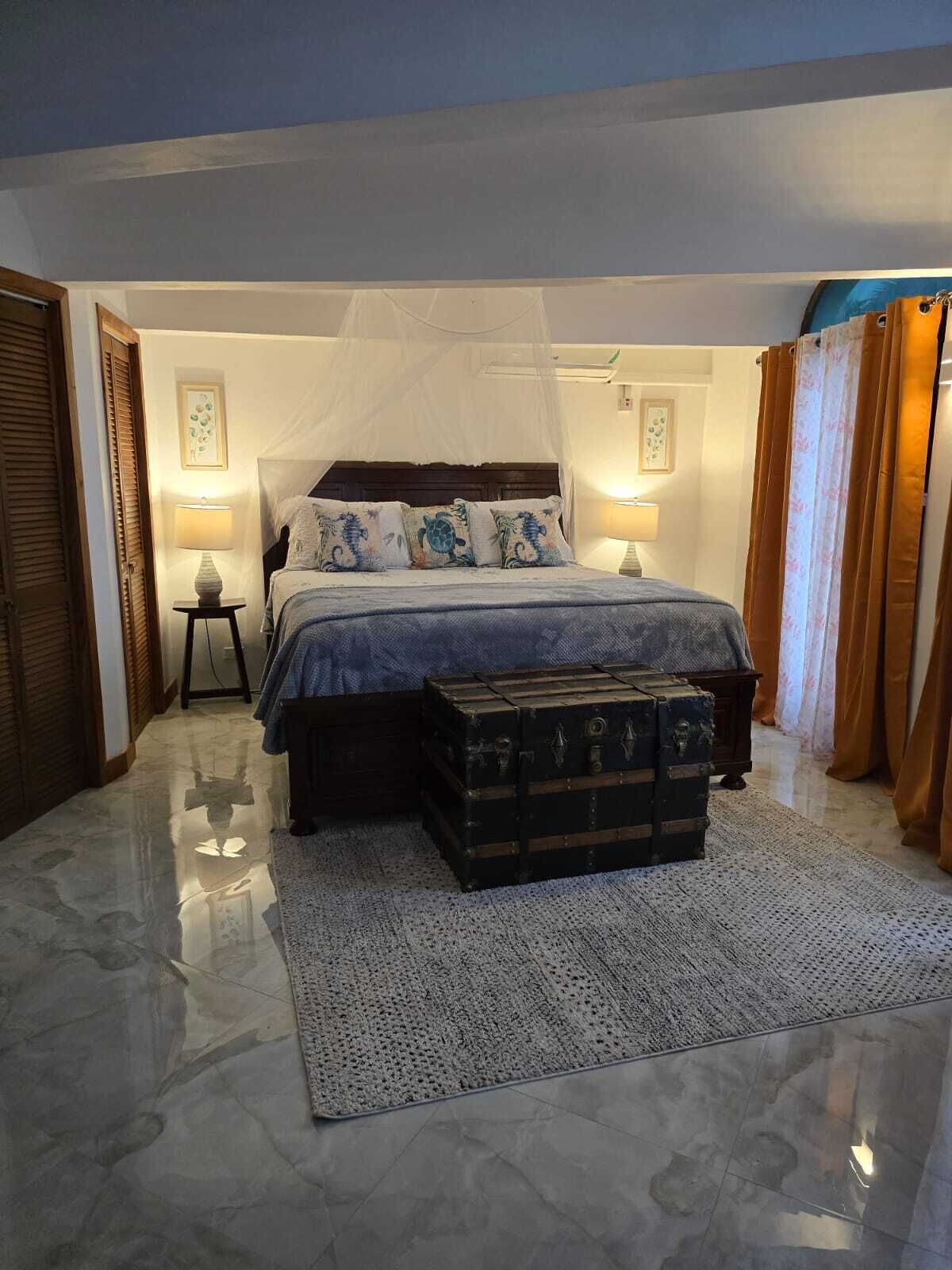 A bedroom with a bed, bedside lamps, a chest of drawers, and a large window.