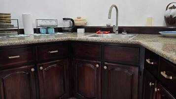 A corner kitchen with dark wood cabinets, a granite countertop, a stainless steel sink, and a small rug.