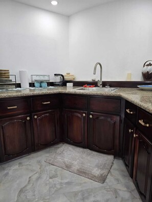 A corner kitchen with dark wood cabinets, a granite countertop, a stainless steel sink, and a small rug.