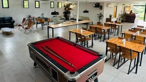 A pool table, dining tables, chairs, and a bar area in a spacious indoor setting.