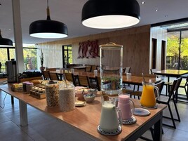 Un comedor moderno con mesas de madera, lámparas colgantes negras y una variedad de recipientes con comida y bebidas.