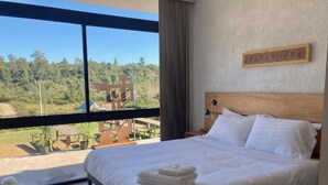 A bedroom with a large bed, a view of the outdoors, and a wooden headboard.