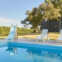 Una piscina con tobogán, sillas de descanso y un área cercada con árboles.