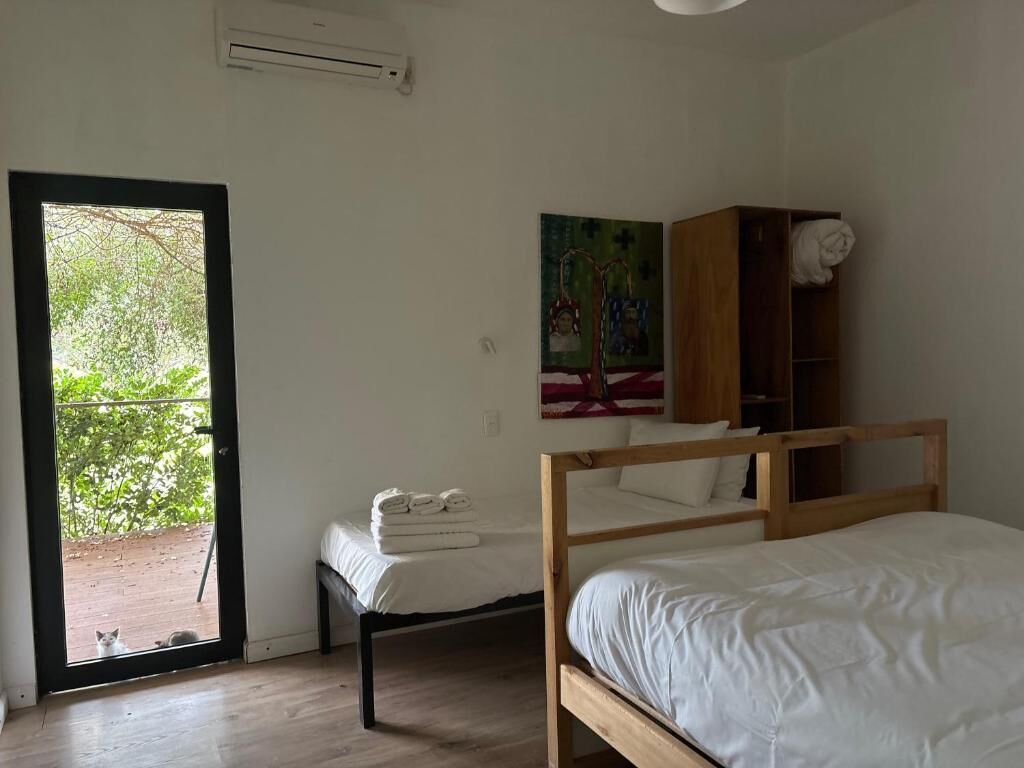 A bedroom with two beds, a wooden wardrobe, a painting, and a door leading to an outdoor area.