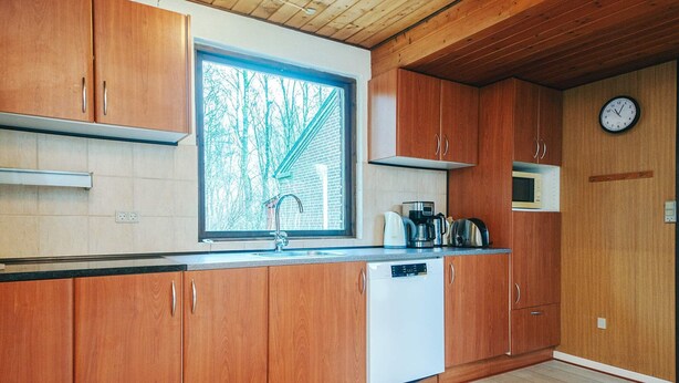 A kitchen with wooden cabinets, a dishwasher, a window with a view of trees, and a clock on the wall. - 10 Person Holiday Home in Herning (Herning)