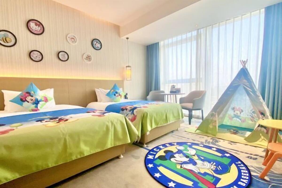 Ein Hotelzimmer mit zwei Betten, einem Mickey-Mouse-Teppich, einem Tipizelt und einem großen Fenster mit Vorhängen.
