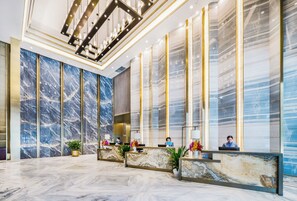 A modern hotel lobby with marble walls, a reception desk, and a chandelier. - Zonhow International Hotel (Hangzhou)
