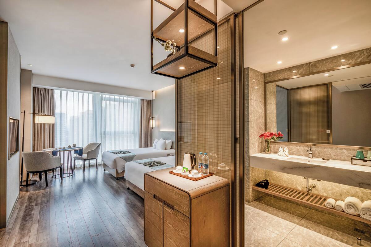 Ein Hotelzimmer mit Bett, Schreibtisch, Stuhl, Schminktisch mit Spiegel und Duschbereich.