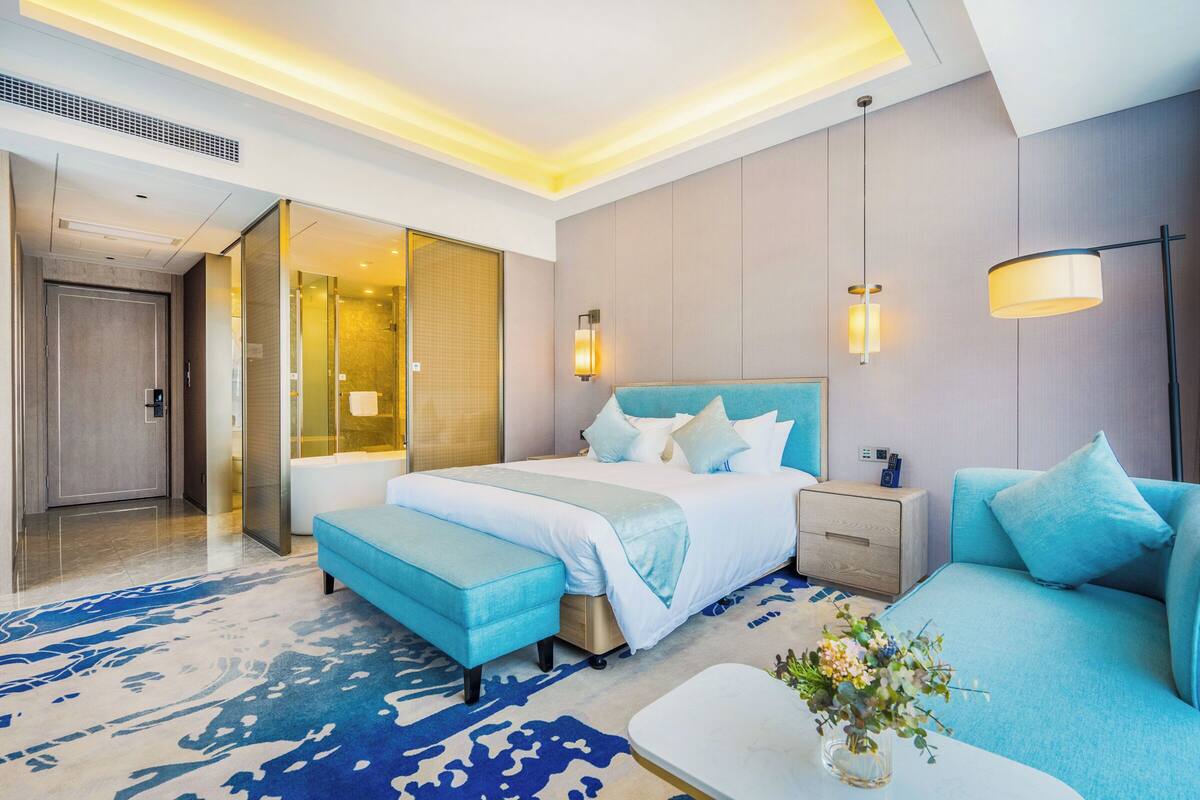 Ein modernes Hotelzimmer mit einem großen Bett, einer Couch, einem kleinen Tisch und einem Badezimmer mit einer Duschkabine.