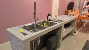Moderni keittiö, jossa on ruostumattomasta teräksestä valmistettu pesuallas, sisäänrakennettu roskakori ja työtaso, jossa on erilaisia esineitä.