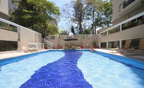 Ein Swimmingpool mit blauem Fliesenmuster, umgeben von Liegestühlen und Topfpflanzen.