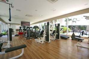 Ein Fitnessraum mit unterschiedlichen Trainingsgeräten, einem Fernseher und großen Fenstern.