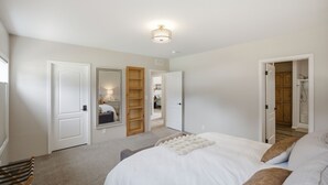 Quarto com cama, um banco de madeira, um guarda-roupa e uma porta que dá para um banheiro.