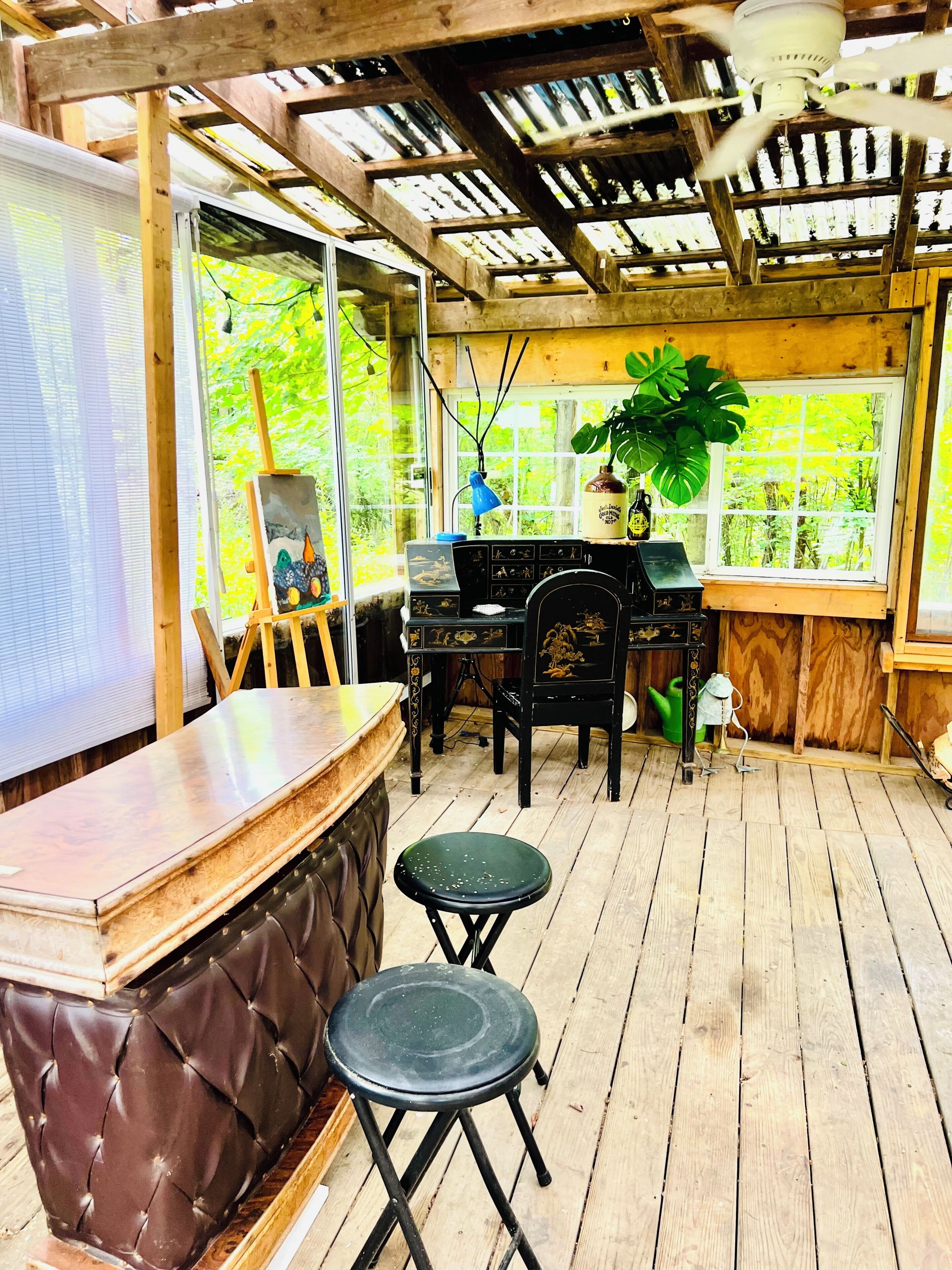 Une terrasse en bois avec un coin bar, une table avec des chaises et une fenêtre donnant sur un paysage verdoyant.