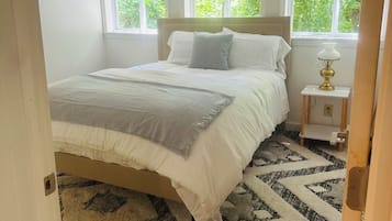 A bedroom with a bed, a nightstand, a lamp, and a window.