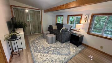 A living room with a sofa, ottomans, a rug, a lamp, and a television.