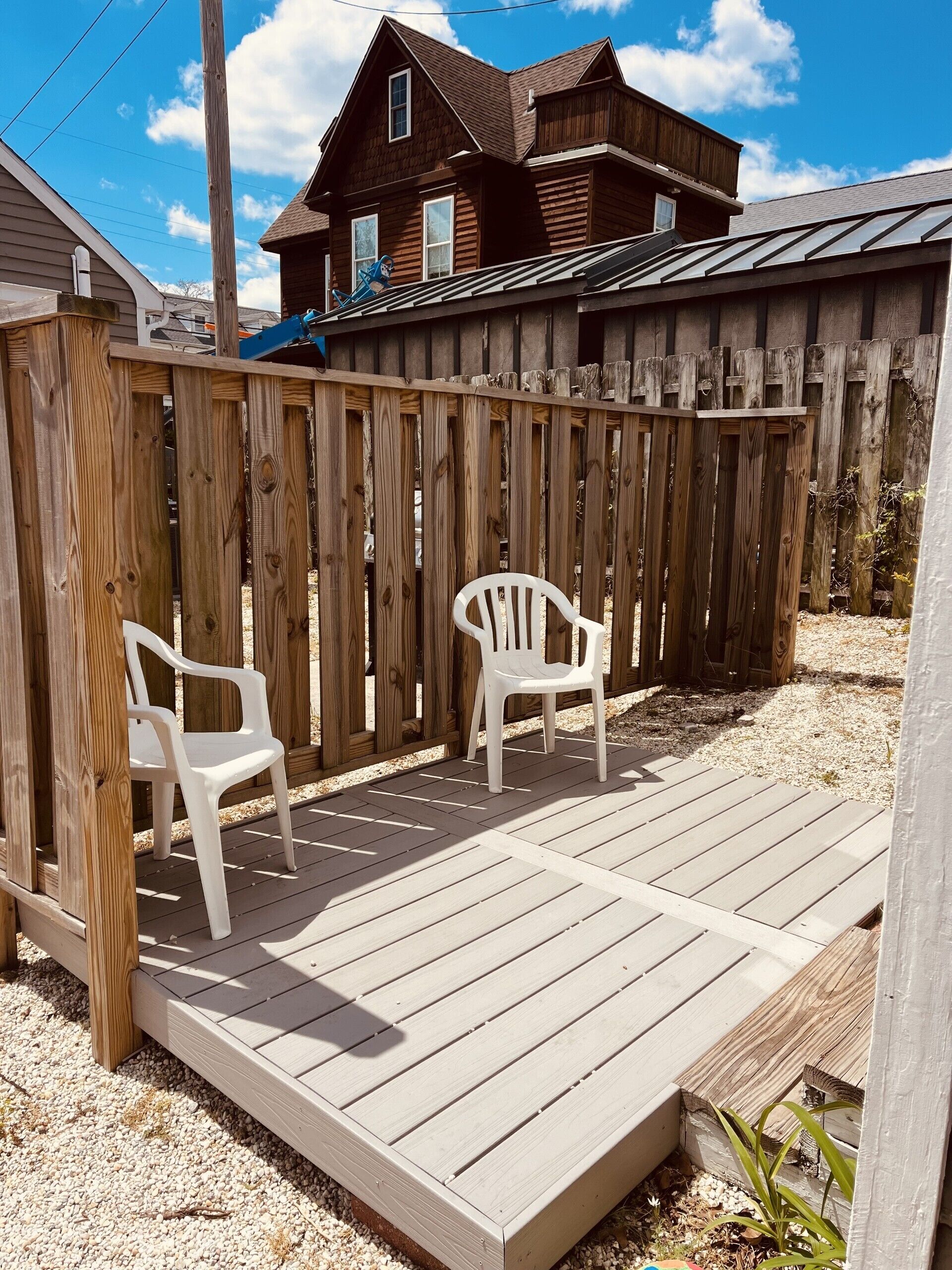 A wooden deck with two white plastic chairs, a wooden fence, and a house in the background.