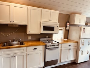 A kitchen with white cabinets, a stainless steel sink, a microwave, an oven, and a refrigerator. - Quiet and charming efficiency Cottage in historic Old Town (Somers Point)
