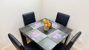 A dining table with four black chairs, a vase with flowers, and a basket of fruits.