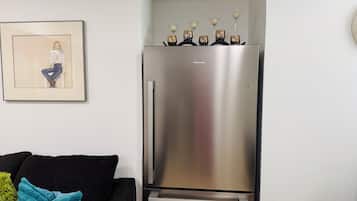 A modern kitchen with a stainless steel refrigerator, a framed artwork on the wall, and a black sofa with a teal throw pillow.