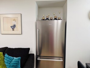Eine moderne Küche mit einem Edelstahl-Kühlschrank, einem gerahmten Kunstwerk an der Wand und einem schwarzen Sofa mit einem türkisfarbenen Kissen.