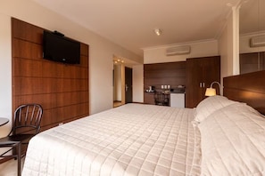 Ein Hotelzimmer mit einem großen Bett, einem an der Wand montierten Fernseher, einer Küchenzeile und einem Sessel.