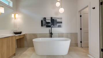 A modern bathroom with a freestanding bathtub, a wooden vanity, a wall-mounted light fixture, and a framed abstract painting.