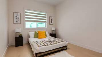 A bedroom with a bed, bedside tables, a window with blinds, and framed artwork on the walls.