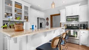 Une cuisine moderne avec des meubles blancs, un plan de travail en granit, des appareils électroménagers en acier inoxydable et un coin bar avec des tabourets.