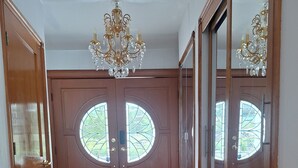 A hallway with wooden flooring, a patterned rug, a double door with glass panels, and a chandelier.