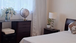 A bedroom with a bed, a dresser, a nightstand, a lamp, a globe, and a window with curtains.