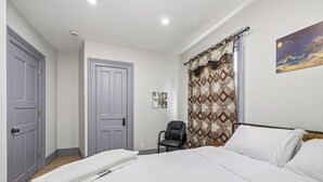 A bedroom with a bed, a chair, a door, and a painting on the wall. - Spacious 6-bedroom house in peaceful Niagara Falls with AC for 22 people sleep (Niagara Falls)