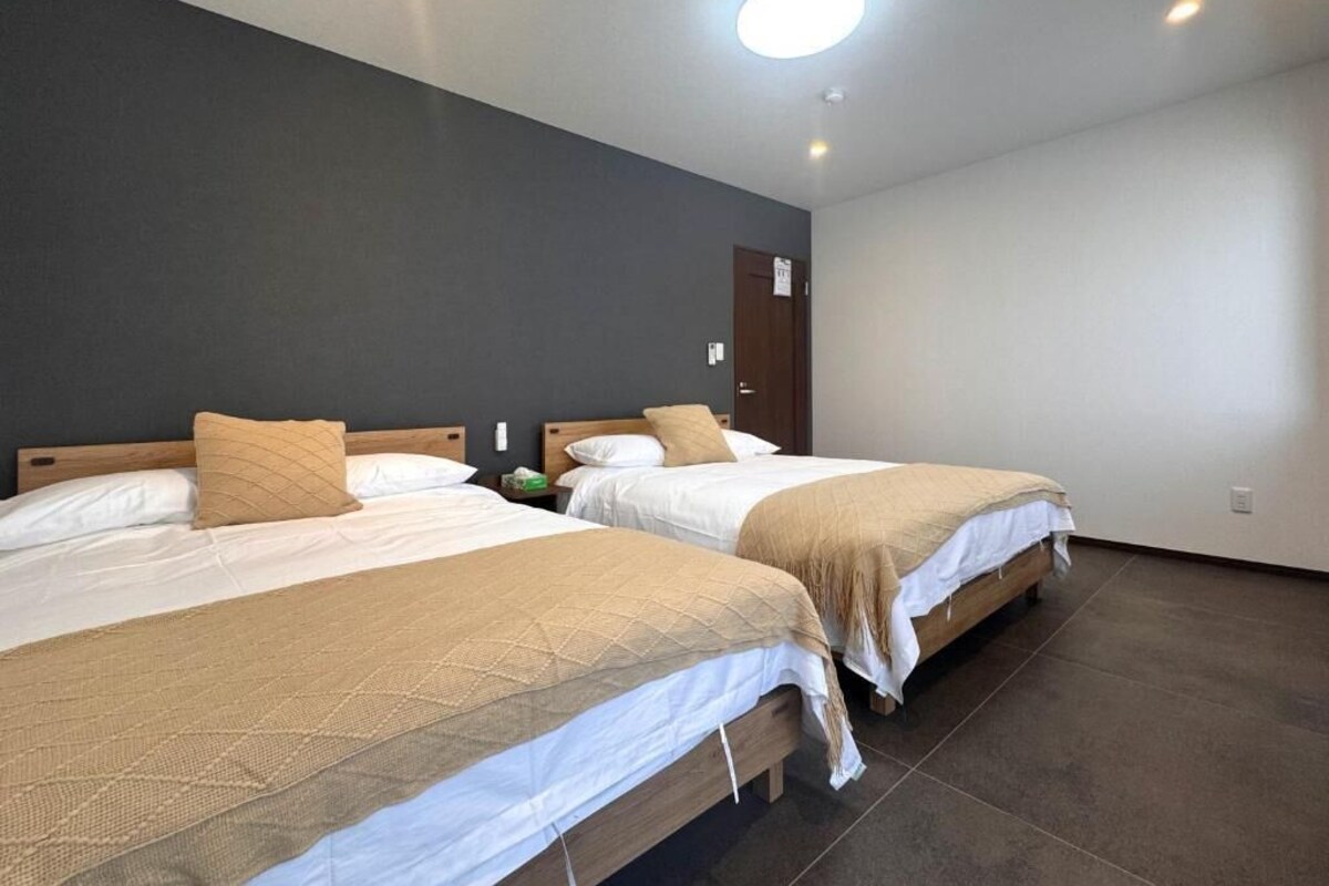Due letti singoli con poggiatesta, una porta in legno e un pavimento piastrellato in una camera d'albergo.