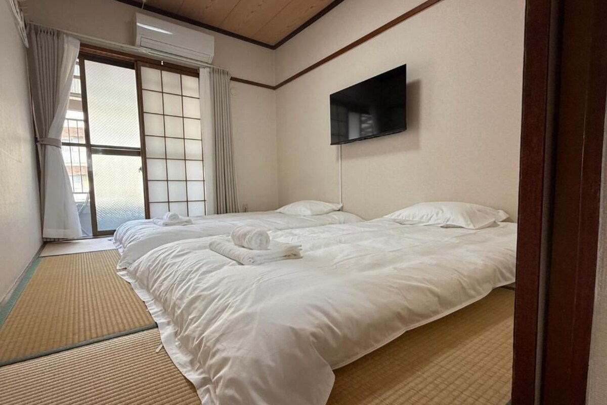 Camera d'albergo con due letti, una TV, tatami e una porta scorrevole.